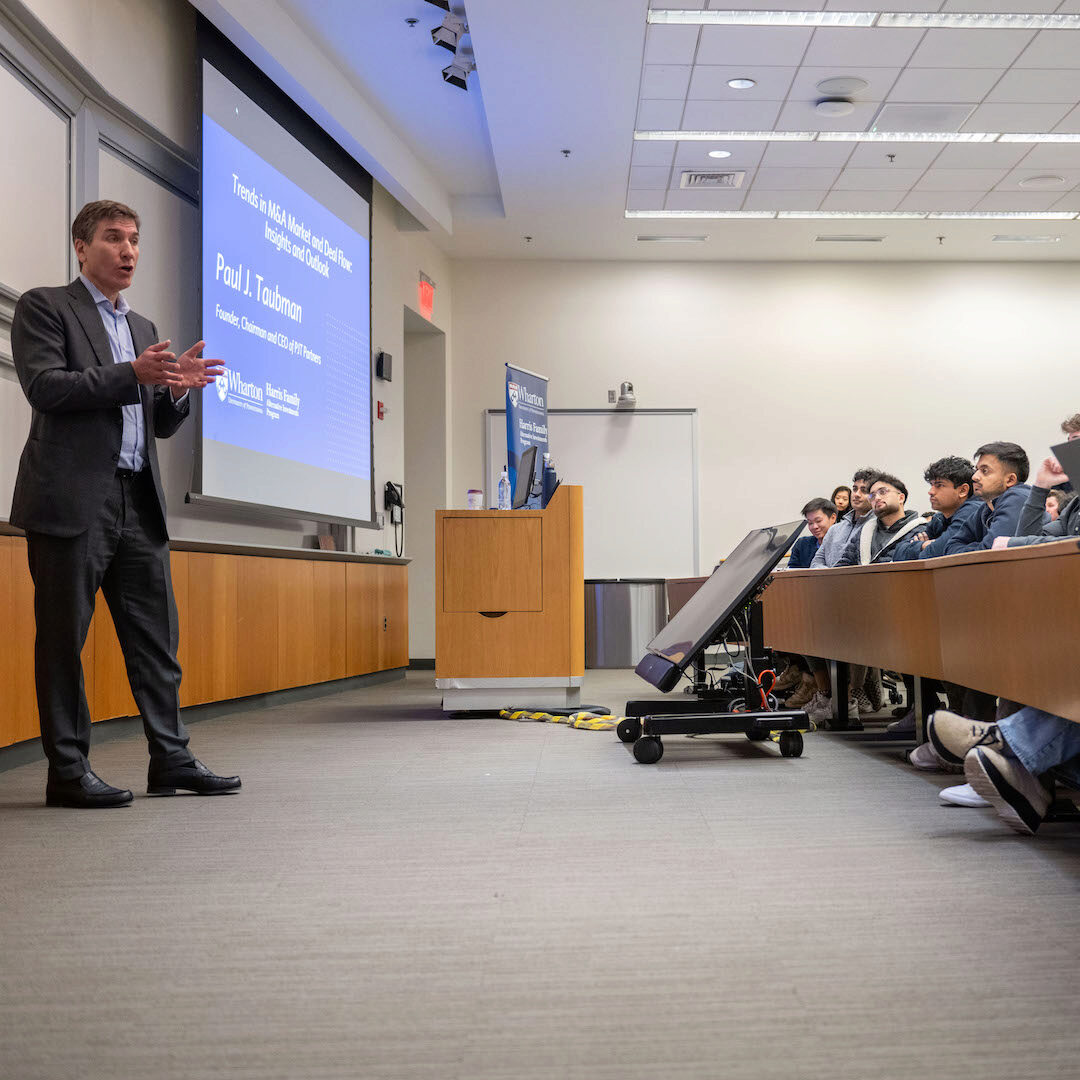 Paul J. Taubman addresses an audience with a blue screen in the background