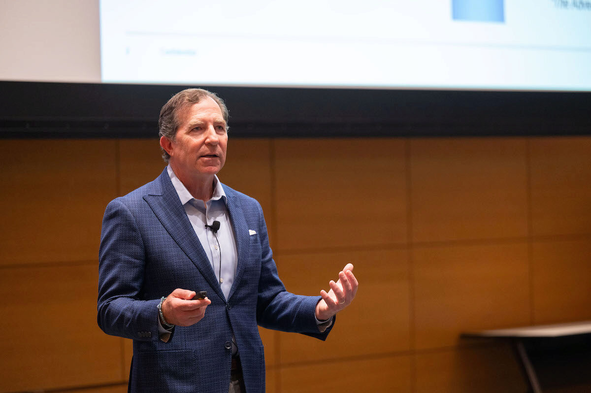 A person speaks, while gesturing with his hands into a lapel microphone in an academic setting