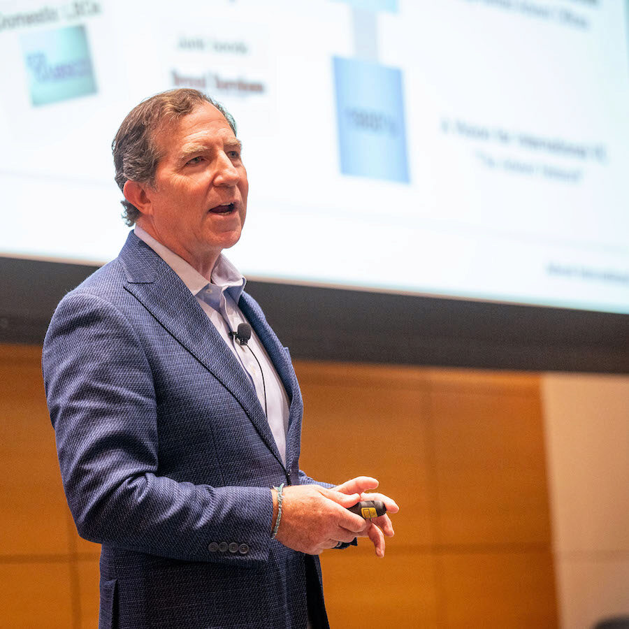 A person speaks, while gesturing with his hands into a lapel microphone in an academic setting