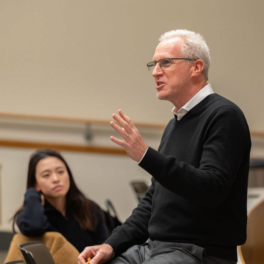 A person sits on a classroom table, as he gives an insightful lecture