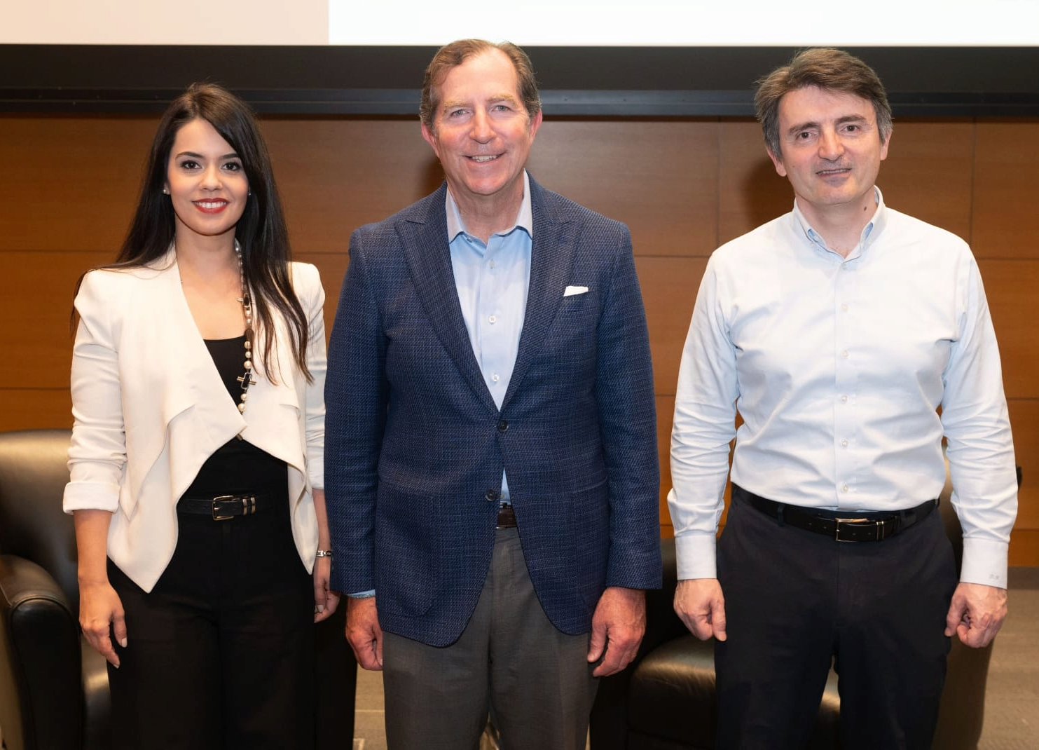 Three people stand smiling toward the viewing, posing for a group photo