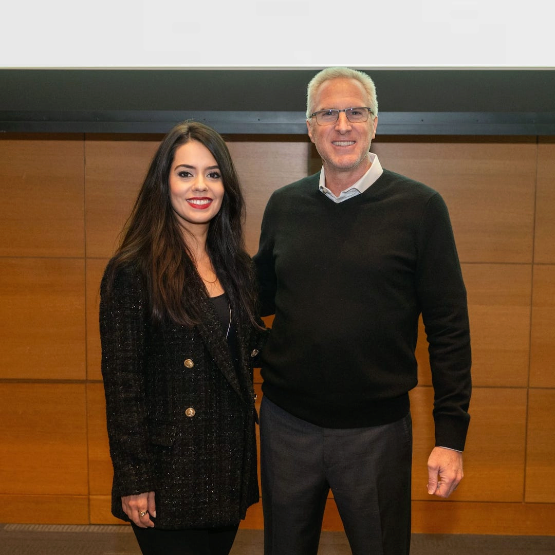 Two people smiling toward the viewer, taking a photograph