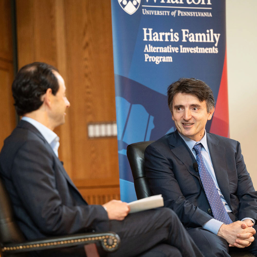 Two people in suits, seated while speaking with one another