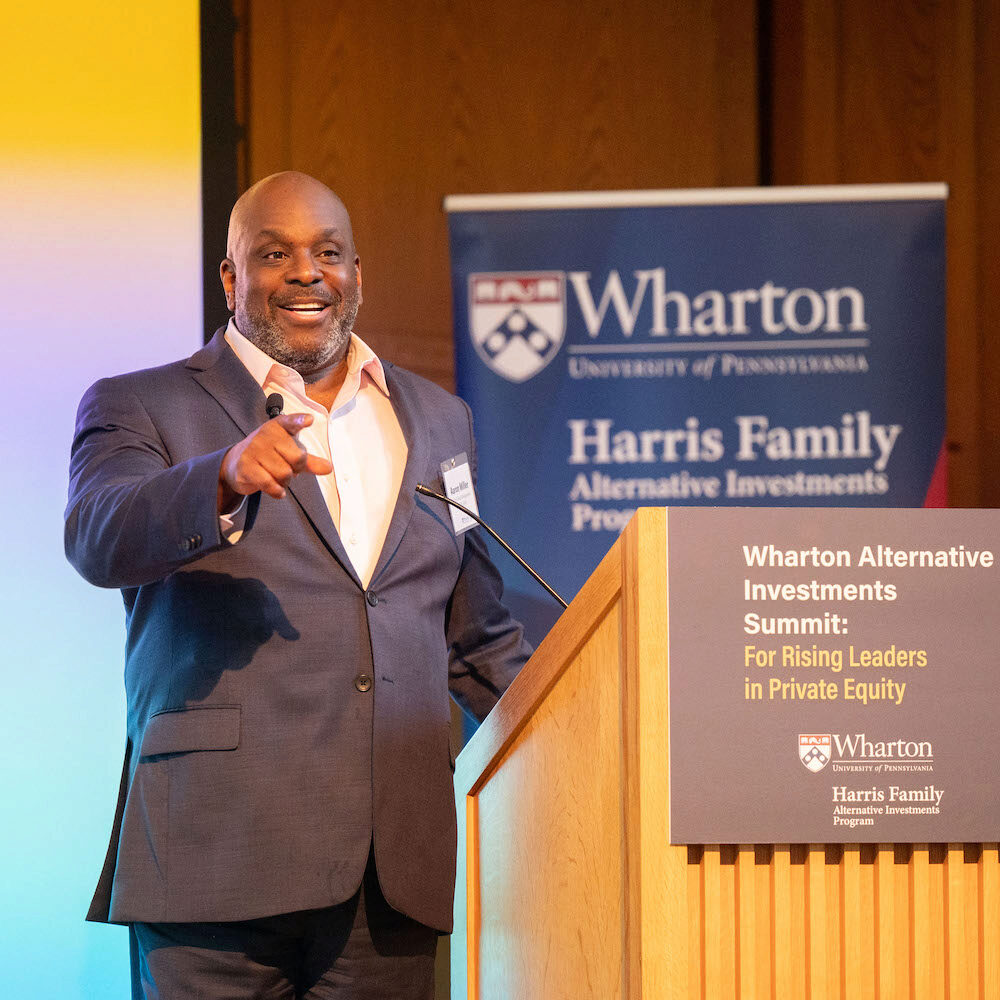 A speaker smiling at a podium, while pointing outward