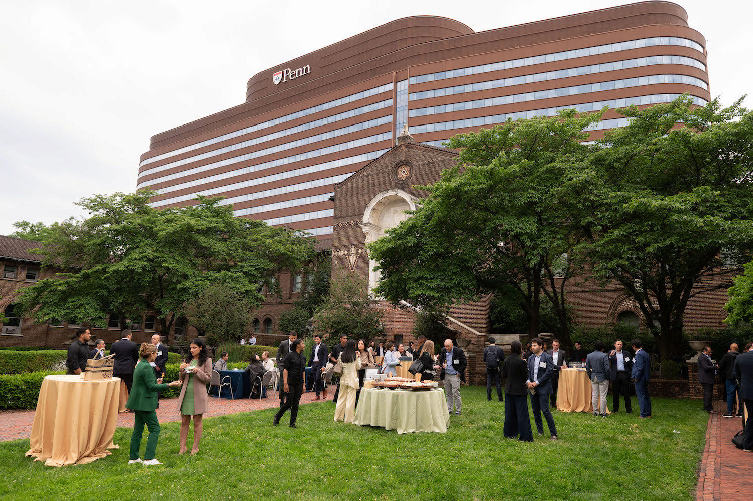 A courtyard with tables and people networking, in front of a large building