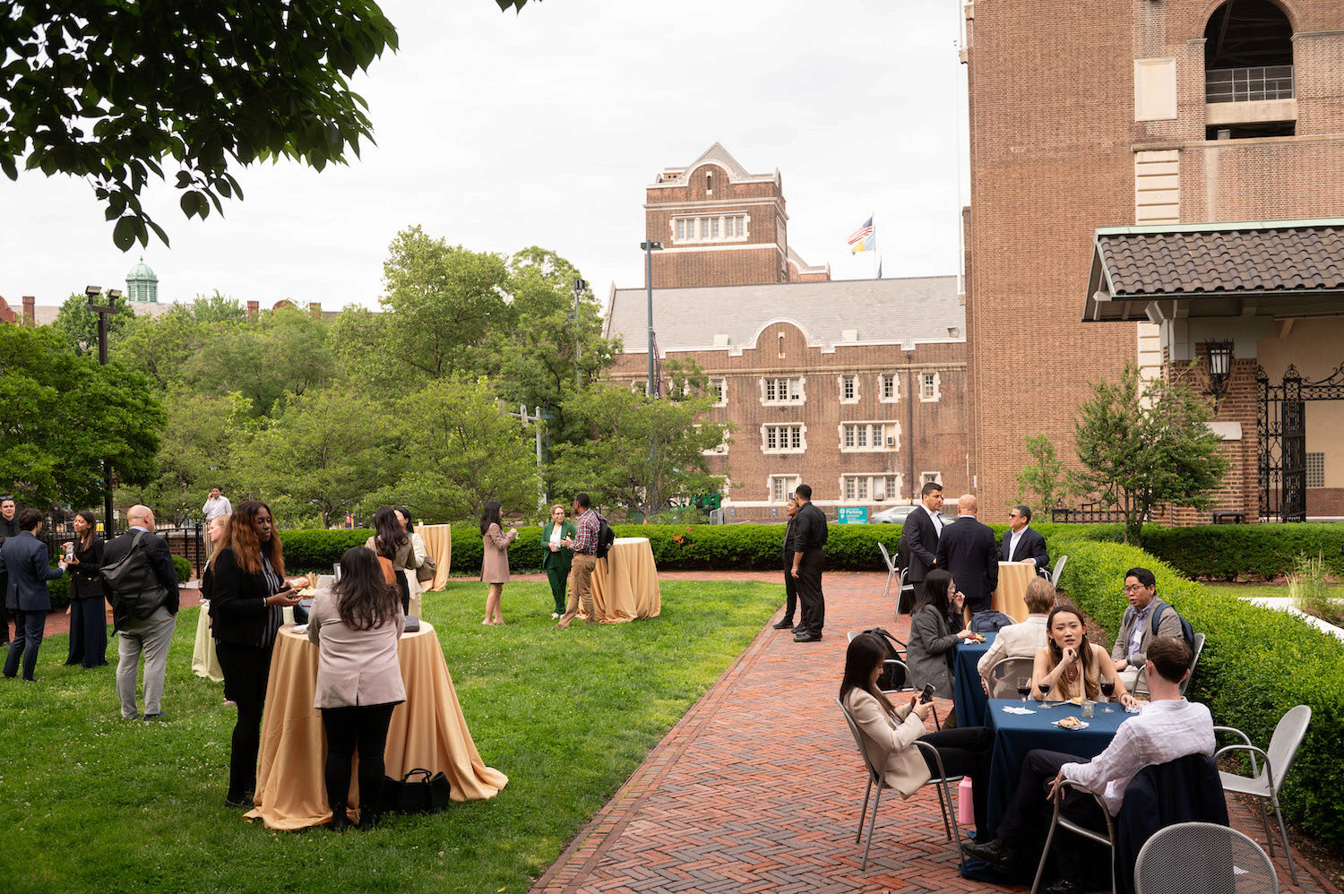 A courtyard with tables and people networking, in front of a large building