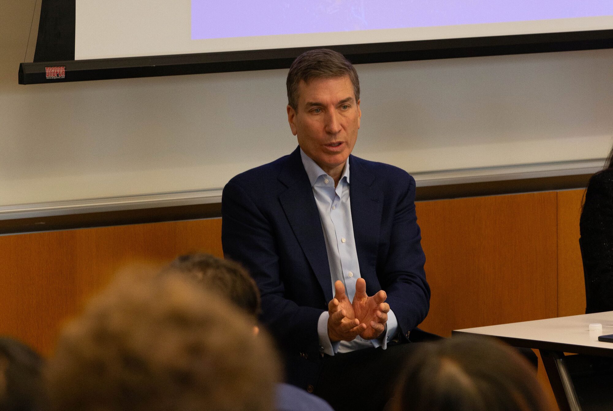 A person gestures while speaking to an audience in an academic setting